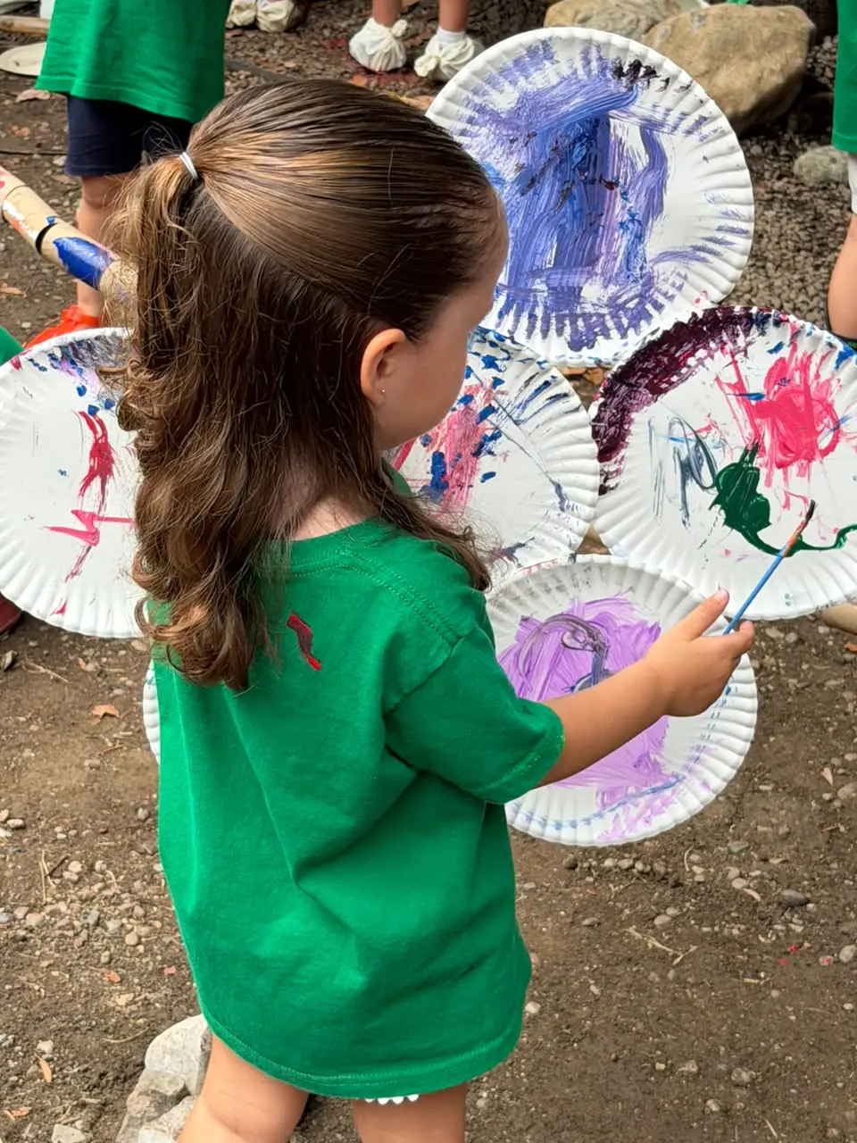 Niña pintando libremente sobre platos de papel al aire libre